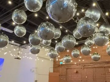 Ceiling decorated with reflective silver balloons and string lights in an industrial space.