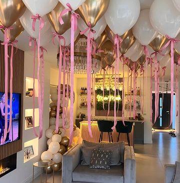Elegant party setup with white and gold balloons and pink ribbons in a modern living room.