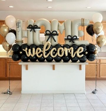Elegant balloon arrangement with "HOME welcome" message in black, white, and gold.