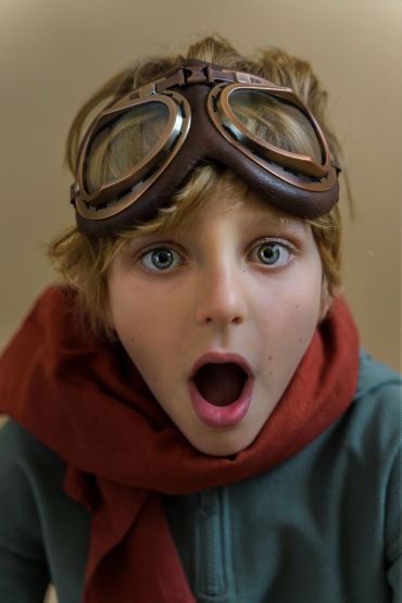 Niño sorprendido con gafas de aviador y bufanda roja.
