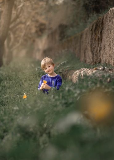 Niño sonriente con camiseta azul entre la vegetación.