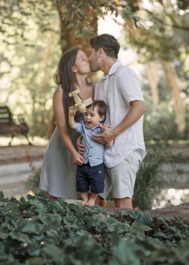 Pareja besándose con niño pequeño en un parque.