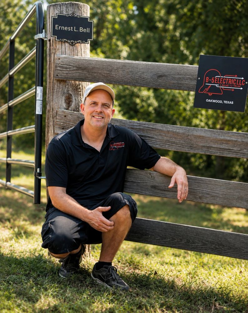Man squatting near a wooden fence with company signs.