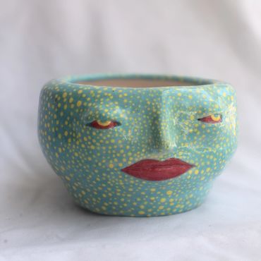 A blue ceramic pot with a face design and yellow dots.