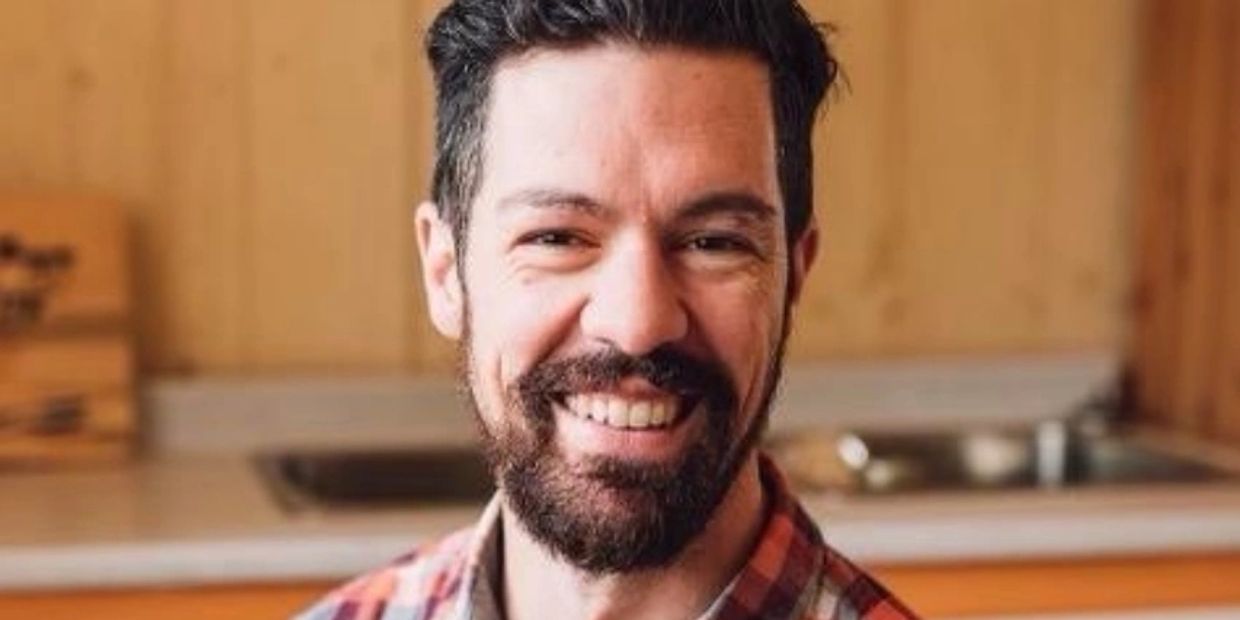 Smiling man with a beard and plaid shirt indoors.