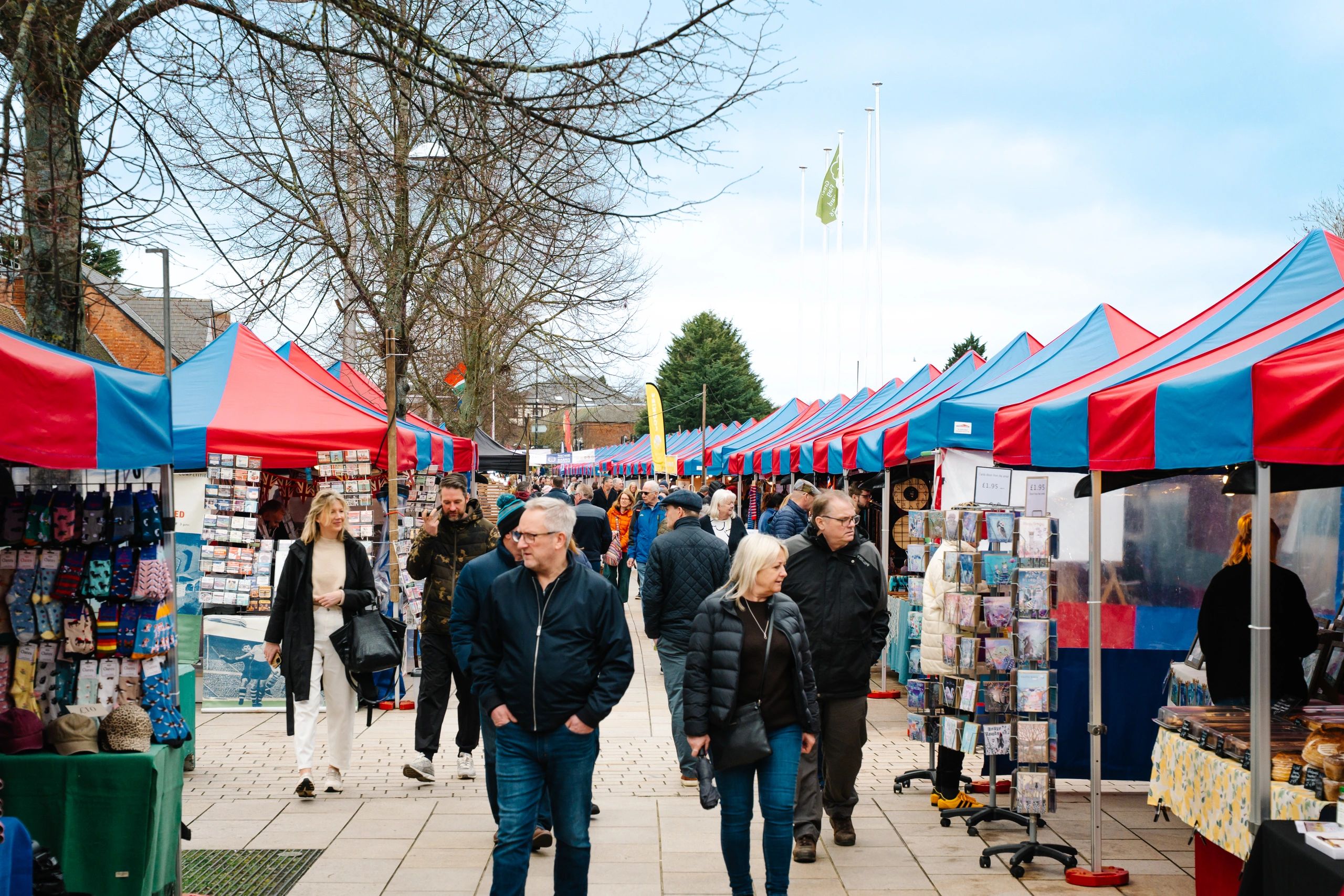 Crowd walking through a bustling outdoor market with red and blue tents.