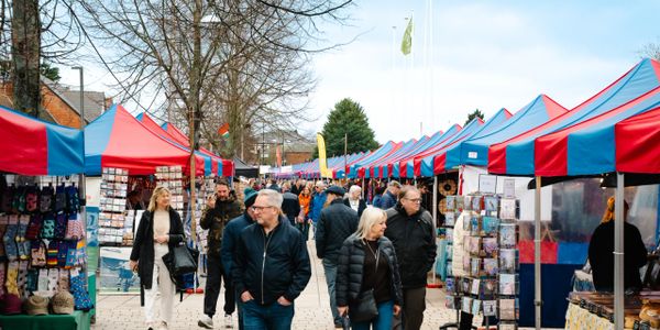 People browse colorful market stalls with red and blue tents on a cloudy day.