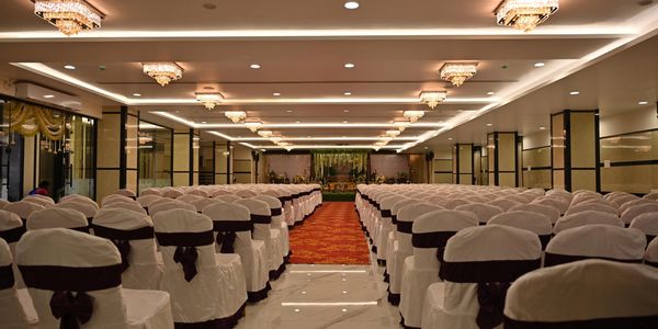 Rows of white-covered chairs with black ribbons in an elegant banquet hall.
