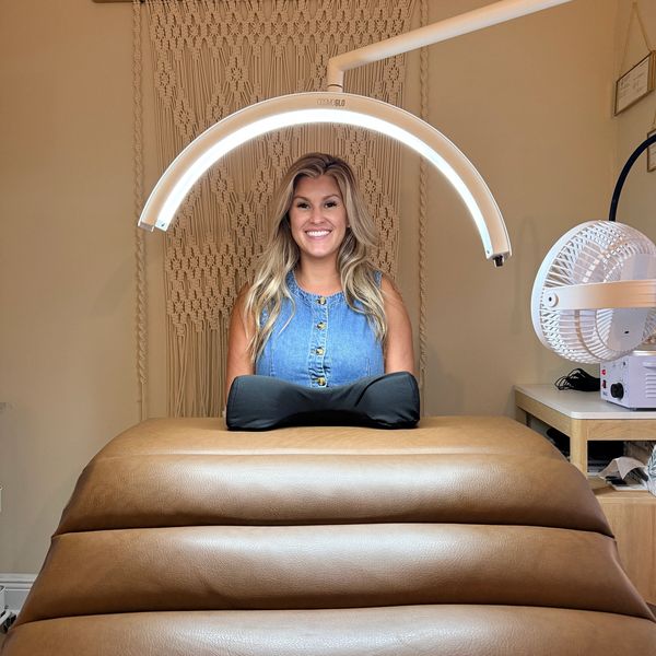 Smiling woman under a ring light in a cozy room.