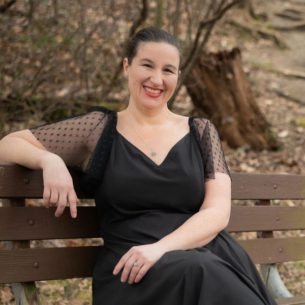 Ashley Biggs is sitting on a park bench in a black dress. 