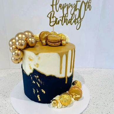 Elegant gold and black 50th birthday cake with macarons and gold accents.