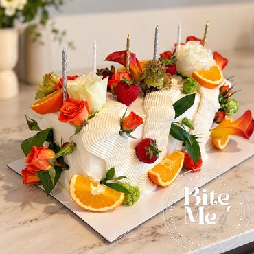 Elegant white cake decorated with fruit, flowers, and candles.