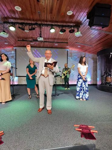 A man passionately speaking on stage with a group and musicians behind him.