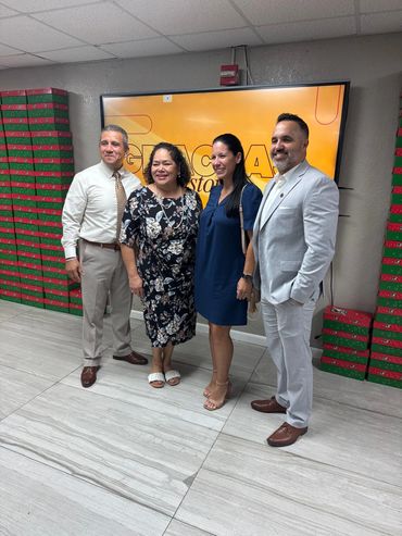 Four people posing indoors against a screen and stacked gift boxes.