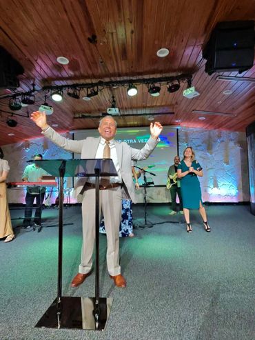 Man speaking passionately at a church service with a worship band behind him.