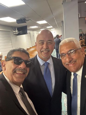 Three smiling men in suits taking a selfie indoors.
