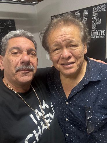 Two older men smiling and posing for a close-up photo indoors.