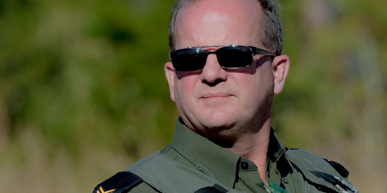 Man wearing dark sunglasses and military uniform outdoors.