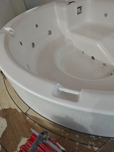 Empty white jacuzzi tub with jets and handles on wooden floor.