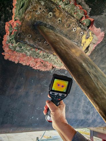 Hand holding thermal camera inspecting a large metallic structure.