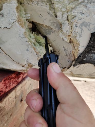 Hand holding a tool near a hole with damage and fibers.