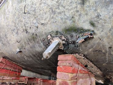 Underside of a boat supported by bricks with barnacles attached.