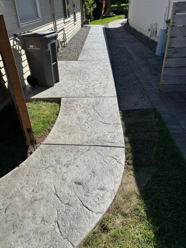 Concrete walkway with curved design beside house.