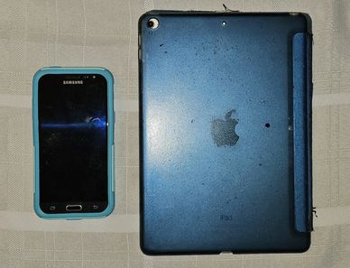 Samsung smartphone and blue Apple iPad placed side by side on a cloth surface.