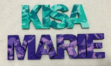 The name Kisa painted in several shades of teal above the name Marie painted in several shades of pu