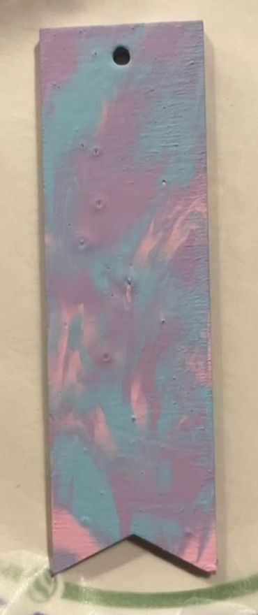 A wooden bookmark with no tassel painted with matte purple, blue, and pink