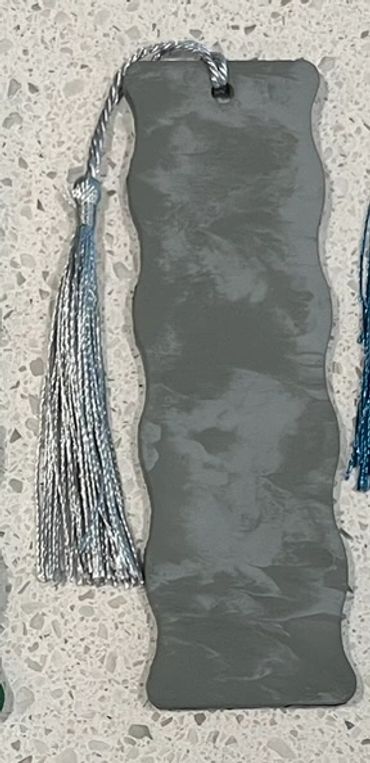 A wooden bookmark painted with two shades of matte gray that has a gray tassel