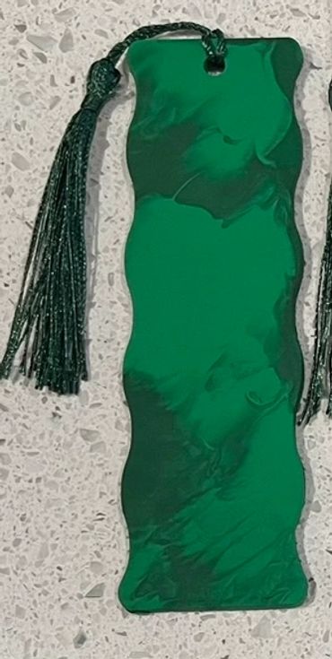 A wooden bookmark painted with two shades of matte green that has a green tassel