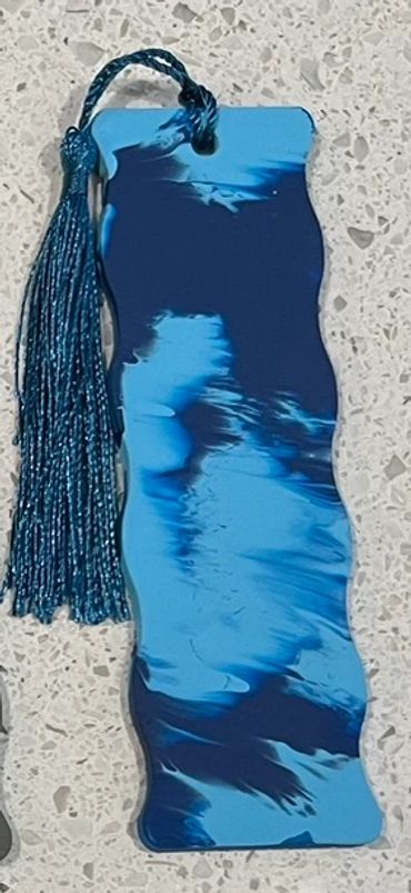 A wooden bookmark painted with two shades of matte blue that has a blue tassel