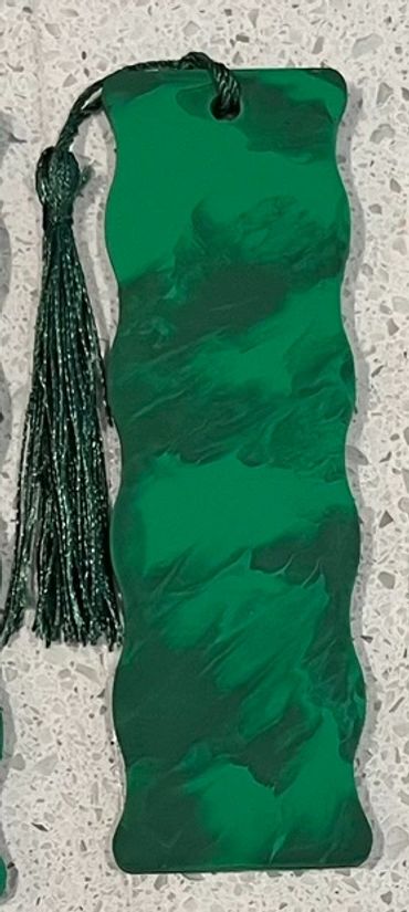 A wooden bookmark painted with two shades of matte green that has a green tassel