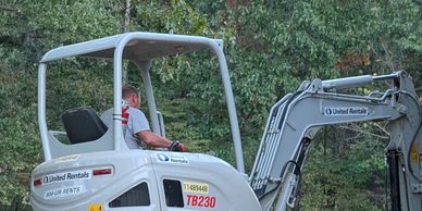 A man operates a TB230 excavator in a green outdoor area.