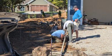 Three men working on a driveway installation outside a house.