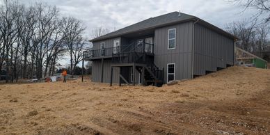Newly constructed gray house on a cleared, dirt-covered lot under a cloudy sky.