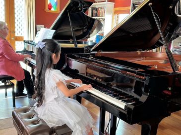 An elderly woman and a young girl playing grand pianos together.