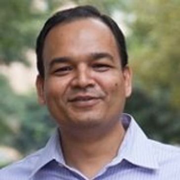 Smiling man outdoors with a light blue shirt.