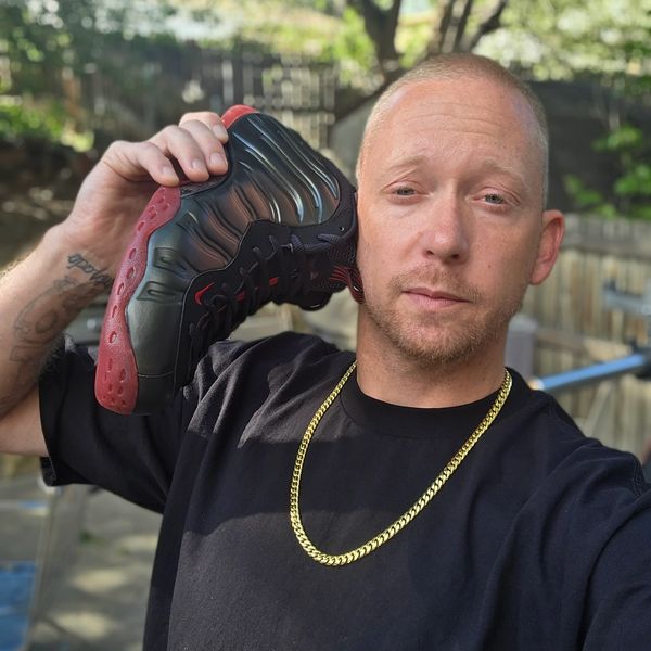 Man holding a black and red sneaker to his ear like a phone.