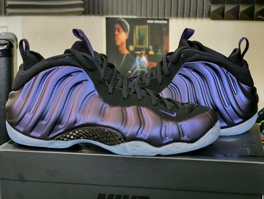 Pair of iridescent purple and black Nike Foamposite sneakers on a box.