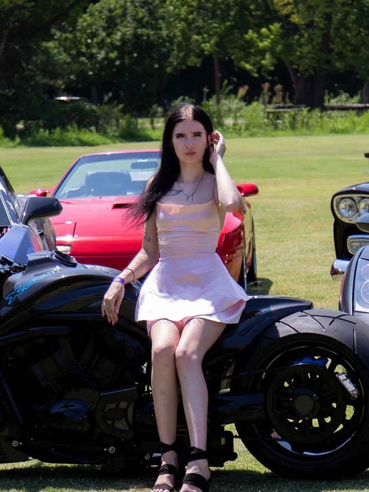 Woman sitting on a black motorcycle outdoors.