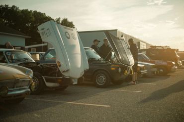 Classic cars with open hoods at a sunny car meet.