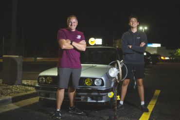 Two young men posing with a car at night.