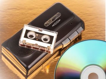 Mini audio cassette sitting on top of a tape player they are sitting next to a CD