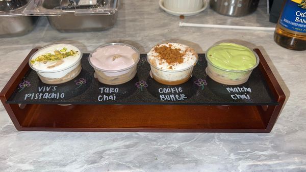 Four flavored dessert samples labeled on a wooden tray.