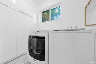 Modern laundry room with washer, dryer, and white cabinetry under a window.