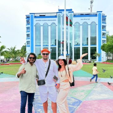 Three friends posing happily in front of a modern building with glass windows.