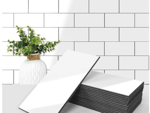 Stack of white rectangular tiles with black edges, next to a white vase with green plants.