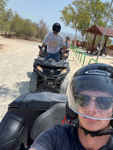 Two people riding all-terrain vehicles on a sunny dirt path.